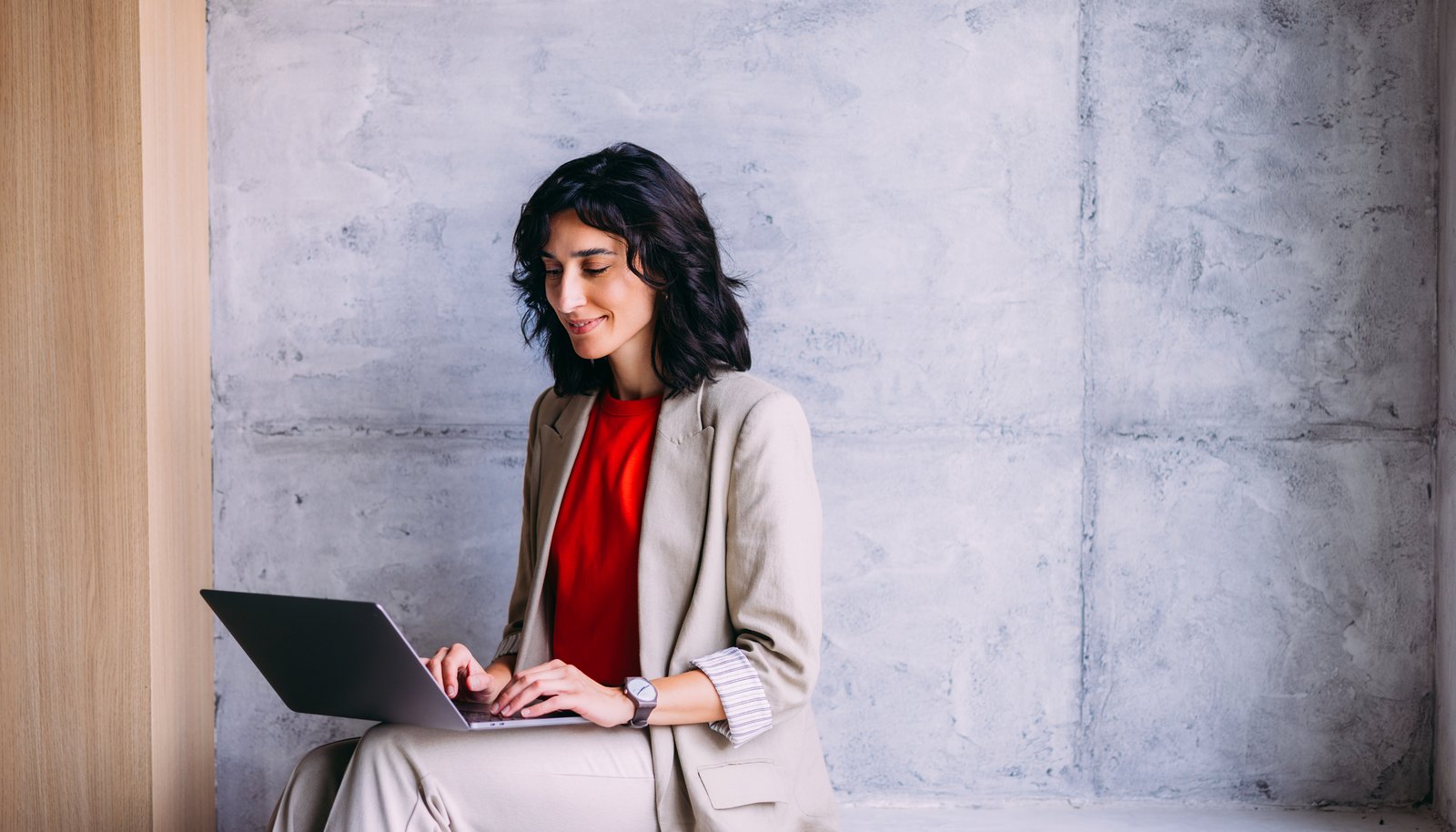 A confident professional in business attire working on a laptop against a clean concrete wall, a non-technical knowledge worker putting AI to work.